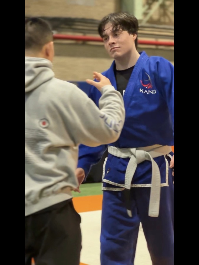 A Kano Martial Arts competitor in a blue gi being coached mat-side before a match